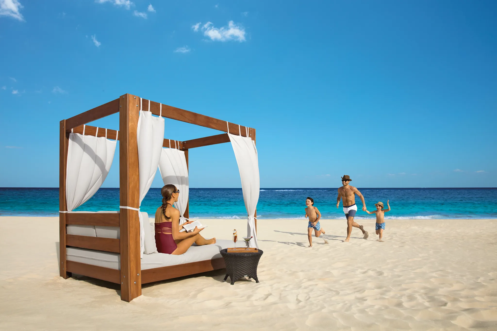 Family relaxing in a beachfront cabana bed with ocean views at Dreams Riviera Cancun Resort & Spa.