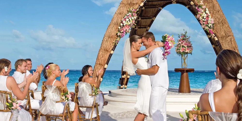 Couple celebrating wedding ceremony under oceanfront gazebo with guests at Dreams Riviera Cancun