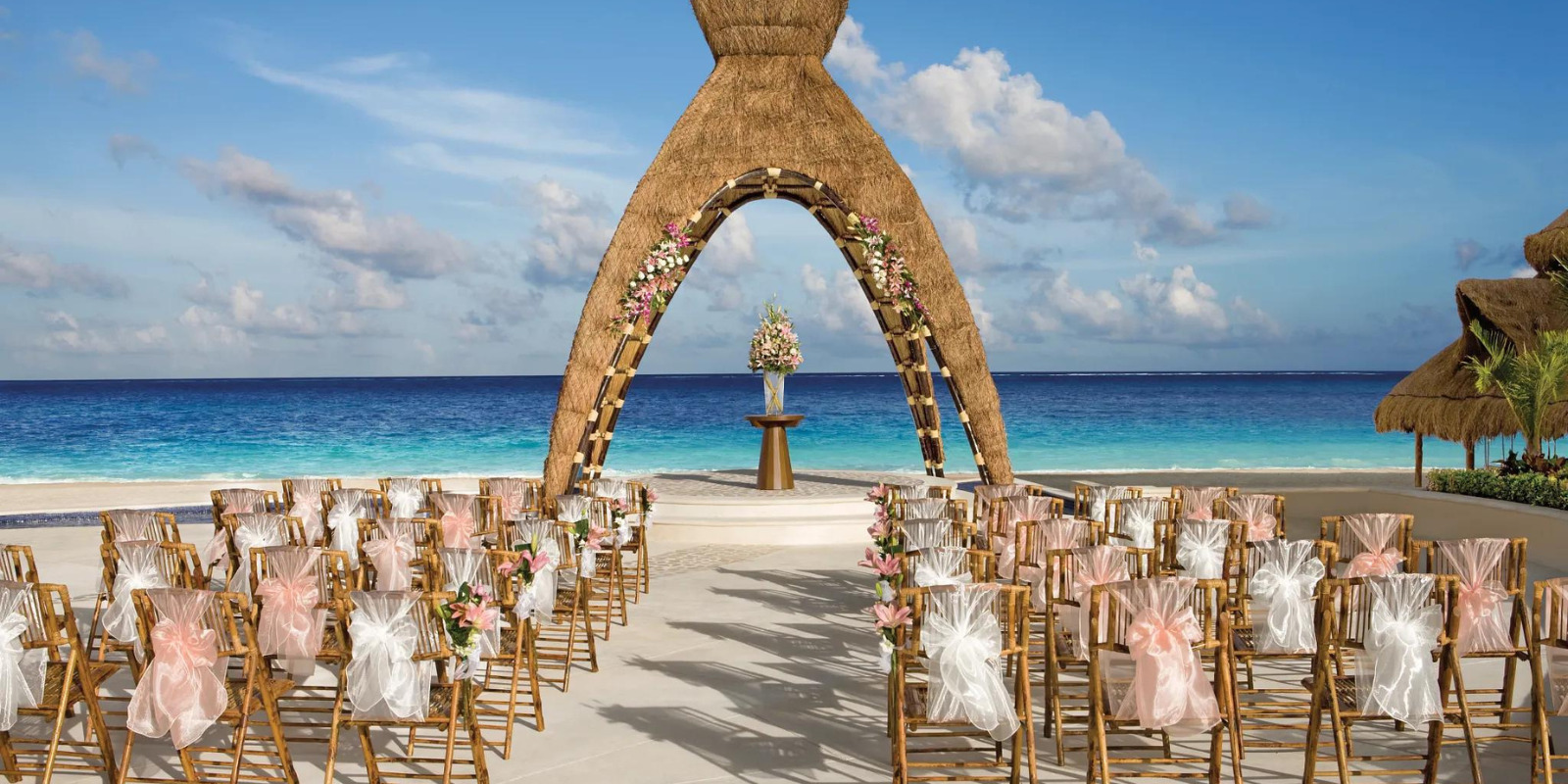 Oceanfront gazebo wedding ceremony with decorated chairs and floral arch at Dreams Riviera Cancun